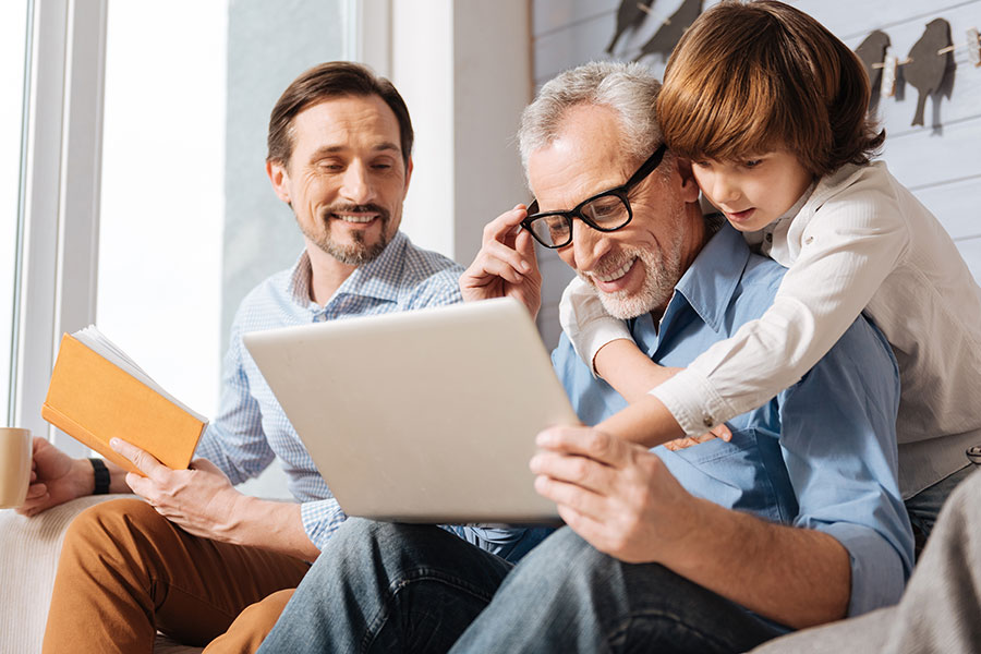 Blog - Grandfather and Grandson Hugging while Looking at Laptop with Father in Background